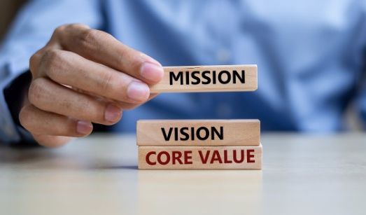 Businessman hand holding wooden building blocks with MISSION, VISION, CORE VALUE Concepts